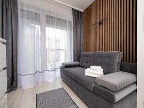 Een moderne woonkamer met een grijze bank, een wand van houten latten, transparante gordijnen en een zwart-wit vloerkleed.