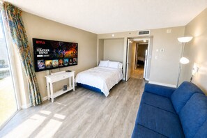 Une chambre d’hôtel avec un lit, un canapé bleu, un téléviseur diffusant une série Netflix et une fenêtre avec des rideaux.