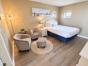 A bedroom with a bed, two armchairs, a nightstand, a lamp, and a painting on the wall.