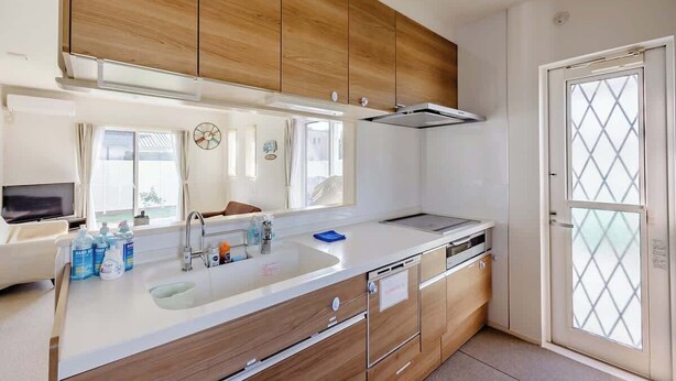 A modern kitchen with wooden cabinets, a white countertop, a built-in oven, and a window with curtains. - Luxury Beach Getaway | Pet-Friendly | BBQ, Sauna & Jacuzzi | Up to 9 Guests (Chōsei, Chōsei District)