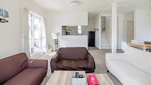 A modern living room with a brown sofa, a white sofa, and a coffee table with a chess set. A kitchen is visible in the background. - Luxury Beach Getaway | Pet-Friendly | BBQ, Sauna & Jacuzzi | Up to 9 Guests (Chōsei, Chōsei District)