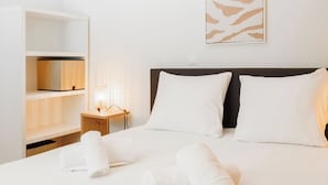 A neatly made bed with white linens and pillows, a bedside table with a lamp, and a wall-mounted abstract art piece. - Beauregard 1 by Interhome (Nendaz)
