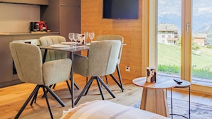 A modern dining area with a table set for four, a television mounted on the wall, and a view of a mountainous landscape through a large sliding door. - Beauregard 1 by Interhome (Nendaz)