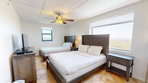 Une chambre avec deux lits, un ventilateur de plafond, une table de chevet, une télévision et une fenêtre donnant sur un paysage agréable.