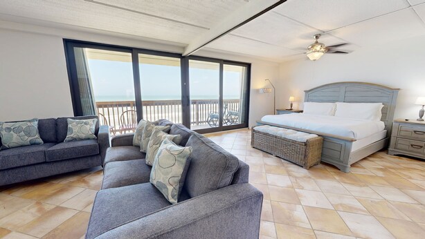 Une chambre spacieuse avec un grand lit, un canapé et un balcon donnant sur la plage.