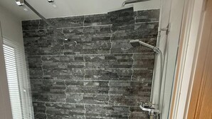 A shower with a glass door, a stone wall, and a white bathtub. - Lakeside Lodge Retreat with Views (Fenstanton)