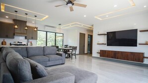 Un salon moderne avec un canapé d’angle gris, un coin repas et un grand téléviseur à écran plat fixé au mur.