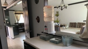 Een moderne keuken met een waterdispenser, een eethoek met een tafel en stoelen, en een woonkamer met een bank en een televisie.