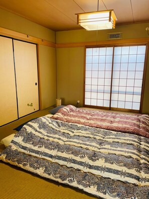 Een traditionele Japanse kamer met tatami vloerbedekking, een shoji-schermraam en een bed met een beddegoed met patroon.