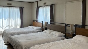 Habitación de hotel con tres camas individuales, una lámpara en el techo, una ventana con cortinas e un equipo de aire acondicionado instalado en la pared.