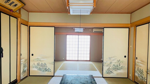 Una habitación japonesa tradicional con suelo de tatami, puertas correderas decoradas con obras de arte y una mesa baja de tatami en el centro.