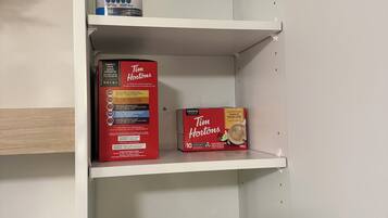 Un meuble blanc avec des étagères contenant une boîte de café Tim Hortons, une boîte de dosettes de café Keurig et un article plié muni d’une sangle noire.