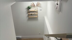 Una escalera con barandilla de madera, un cartel de bienvenida y una planta pequeña en la pared.