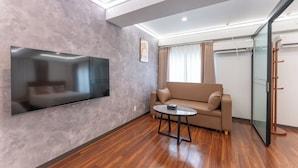 Un salon moderne avec un téléviseur à écran plat fixé à un mur texturé, un canapé beige, une petite table ronde et une cloison en verre.