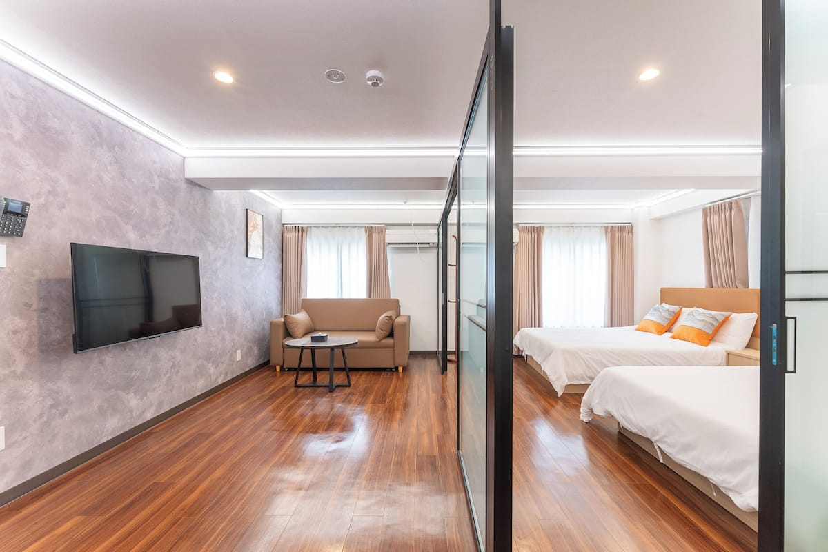 Quarto de hotel moderno com televisão de tela plana, um sofá, duas camas e um painel de vidro.