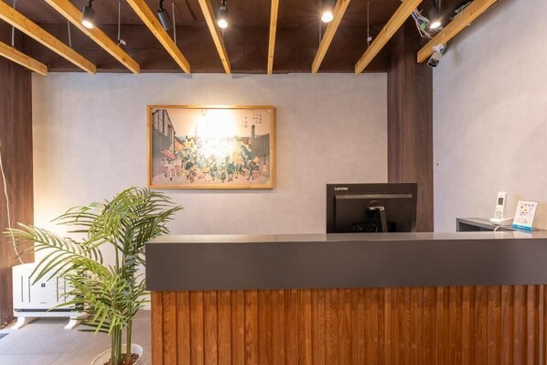 A reception desk with a framed artwork above it, a potted plant to the left, and a Lenovo device on the right.