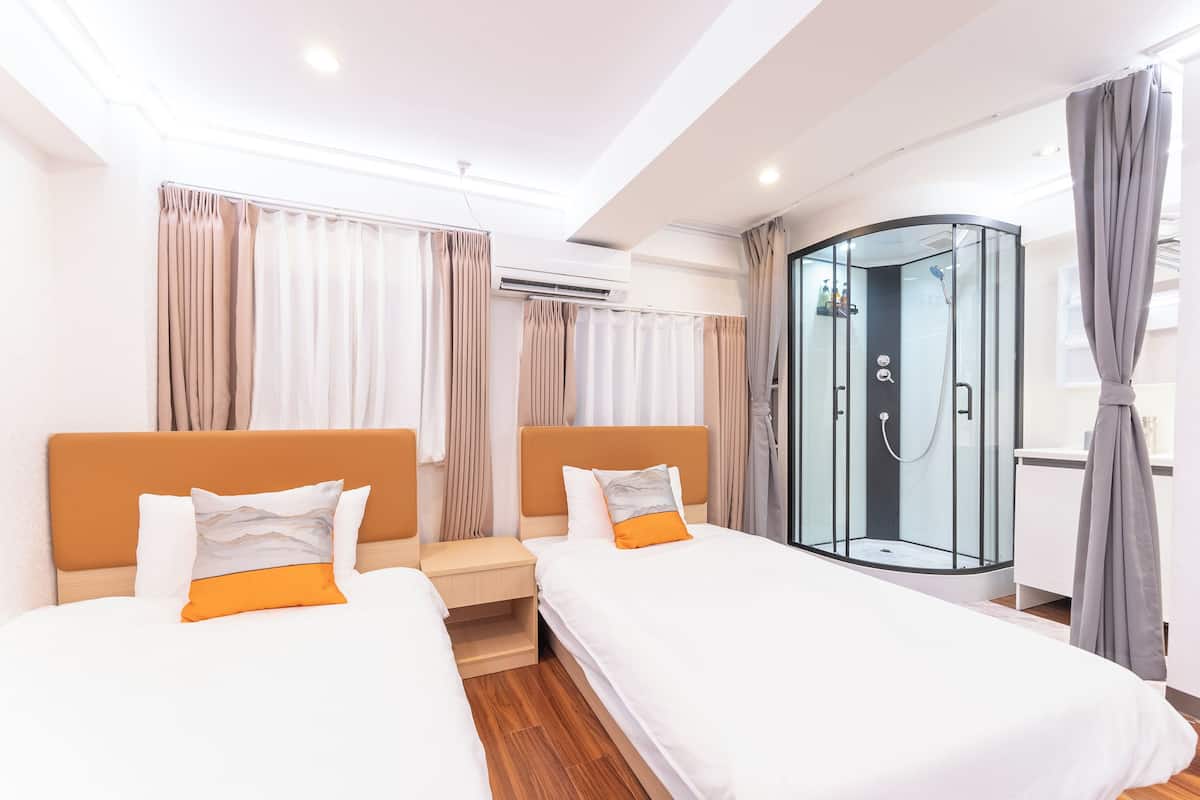 Quarto de hotel com duas camas, um chuveiro em gabinete de vidro e piso de madeira.