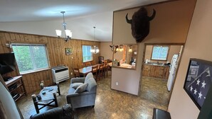 A spacious living area with a television, sofa, and dining table. A bull head decoration is mounted on the wall. - Enchanting cabin on the river in charming Anchor Point, AK (Anchor Point)