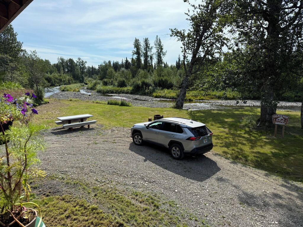 Un espace de stationnement recouvert de gravier, avec une table de pique-nique et une voiture.