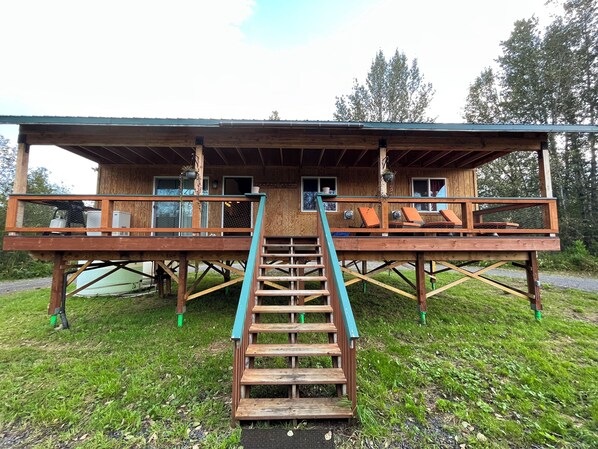 A wooden cabin with a deck and a staircase leading to a balcony. - Enchanting cabin on the river in charming Anchor Point, AK (Anchor Point)