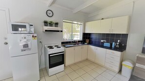 A compact kitchen with white appliances, a gas stove, and a window. - Esperance Little Units 1 (Castletown)