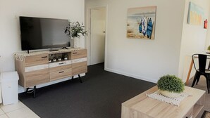 A modern living room with a flat-screen TV, wooden furniture, a small plant, and a painting on the wall. - Esperance Little Units 1 (Castletown)