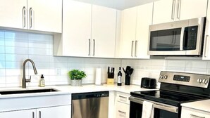 Una cocina moderna con gabinetes blancos, electrodomésticos de acero inoxidable, lavavajillas, microondas y horno.