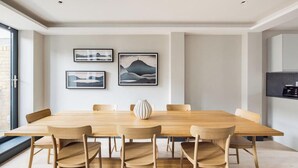 A modern dining area with a wooden table and chairs, framed artwork on the wall, and a kitchen area visible to the right. - The Covent Garden Maison — 4‑Bed Duplex Sleeps 8 (London)