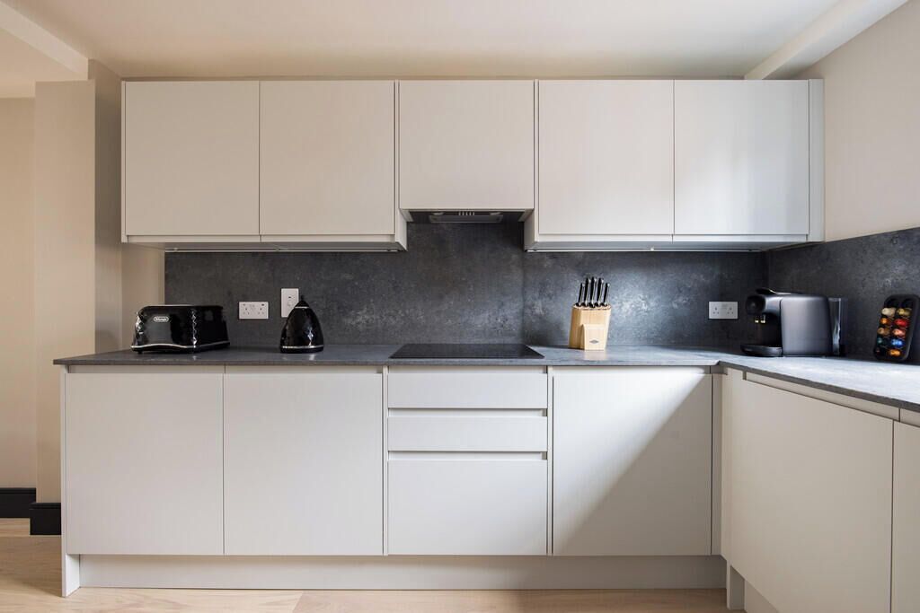 Una cocina moderna con armarios blancos, encimera negra y una cafetera.