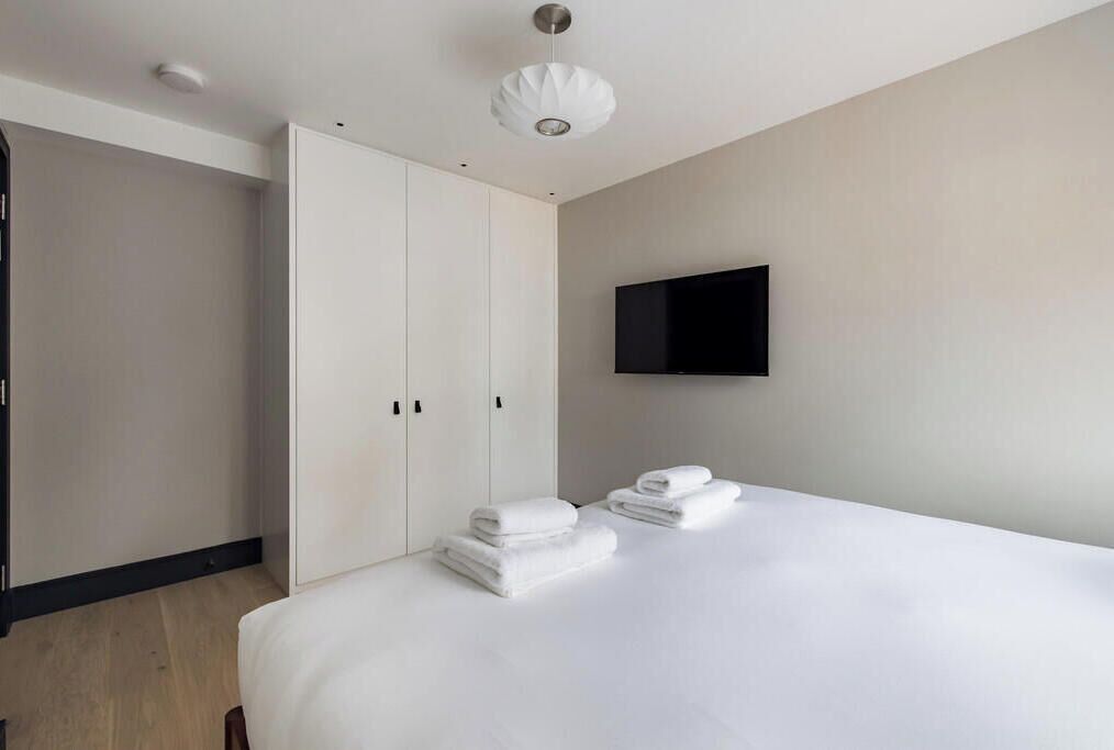 Una habitación de hotel moderna con una cama grande, un armario y un televisor de pantalla plana montado en la pared.