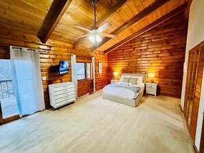 A log cabin bedroom with a bed, bedside tables, a TV, and a ceiling fan.