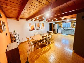 A spacious dining area with a wooden table and chairs, a kitchen in the background, and artwork on the walls.
