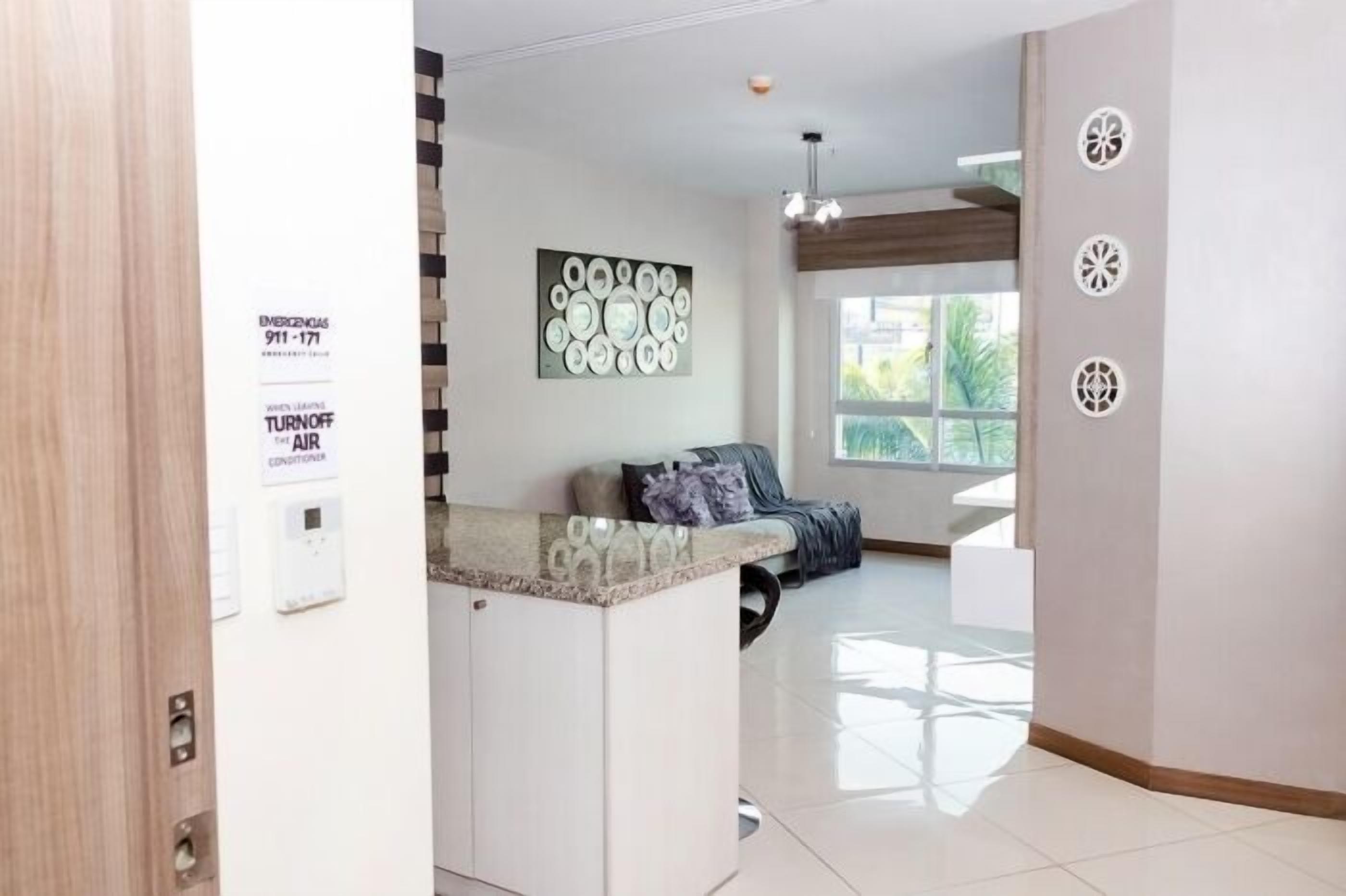 Un interior moderno con cocina, zona de estar con sofá y mesa de centro, y ventana que proporciona luz natural.