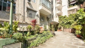 A stone pathway leading to a building with multiple balconies and a variety of potted plants and flowers.