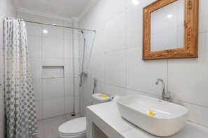 A bathroom with a shower, toilet, and sink with a mirror above. - The Tis Guesthouse and Hostel (Canggu)