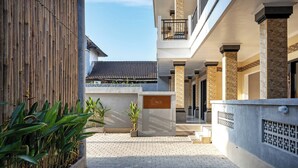 A courtyard with a bamboo fence, potted plants, and a building with a sign reading "THE TIS". - The Tis Guesthouse and Hostel (Canggu)