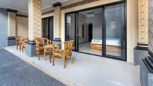 A hotel room with a large sliding glass door, a bed, and a seating area with wooden chairs and a table. - The Tis Guesthouse and Hostel (Canggu)