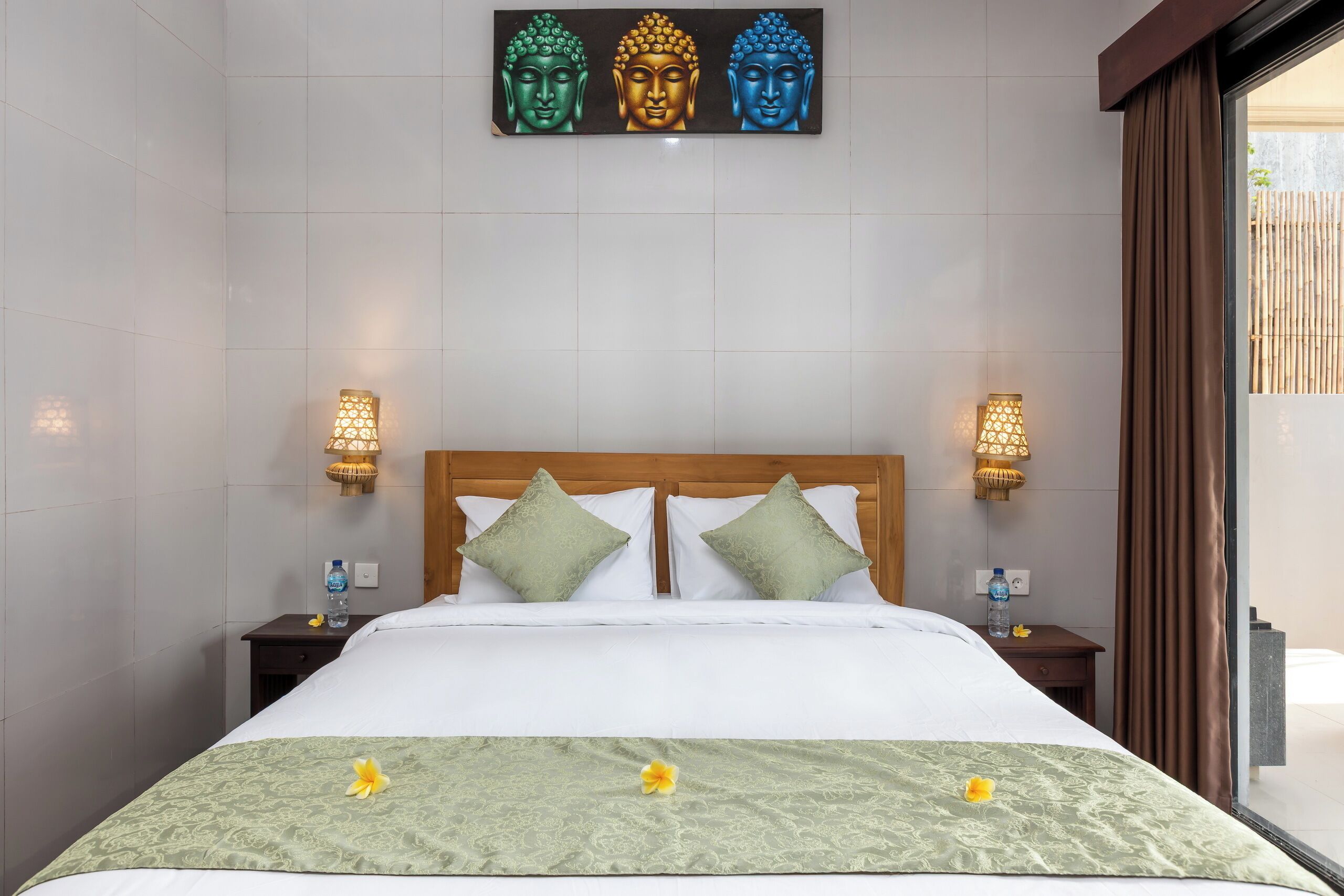Habitación de hotel con una cama grande, dos mesitas de noche, una obra de arte de Buda en la pared y vistas al exterior.