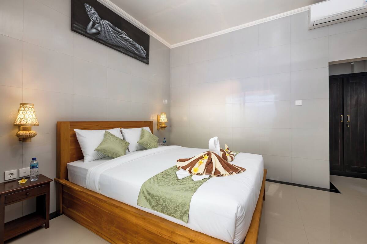 A hotel room with a wooden bed, white linens, a green throw blanket, and a Buddha painting on the wall.