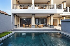 Uma casa moderna de dois andares com piscina, área de estar externa e uma varanda com cadeiras de vime.