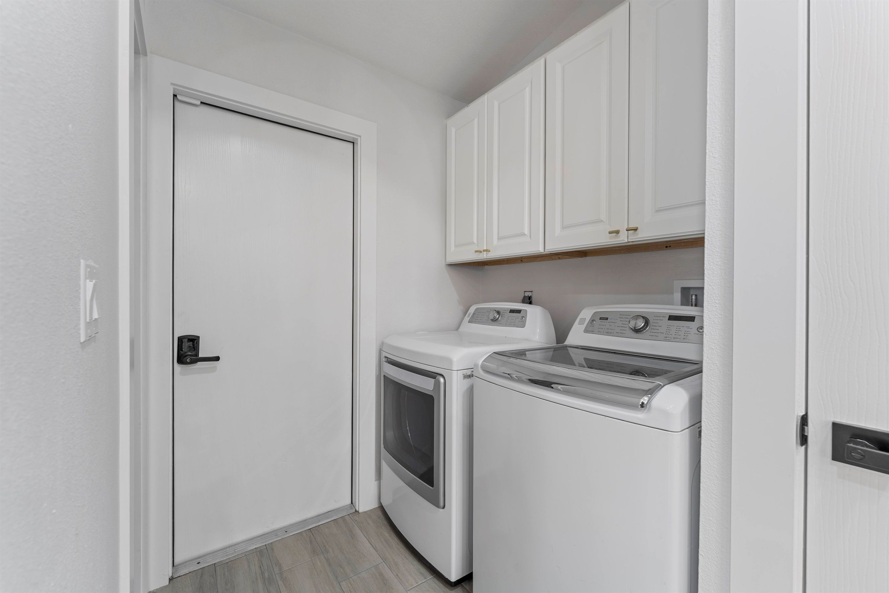 A laundry room with a door, two washing machines, and white cabinets.