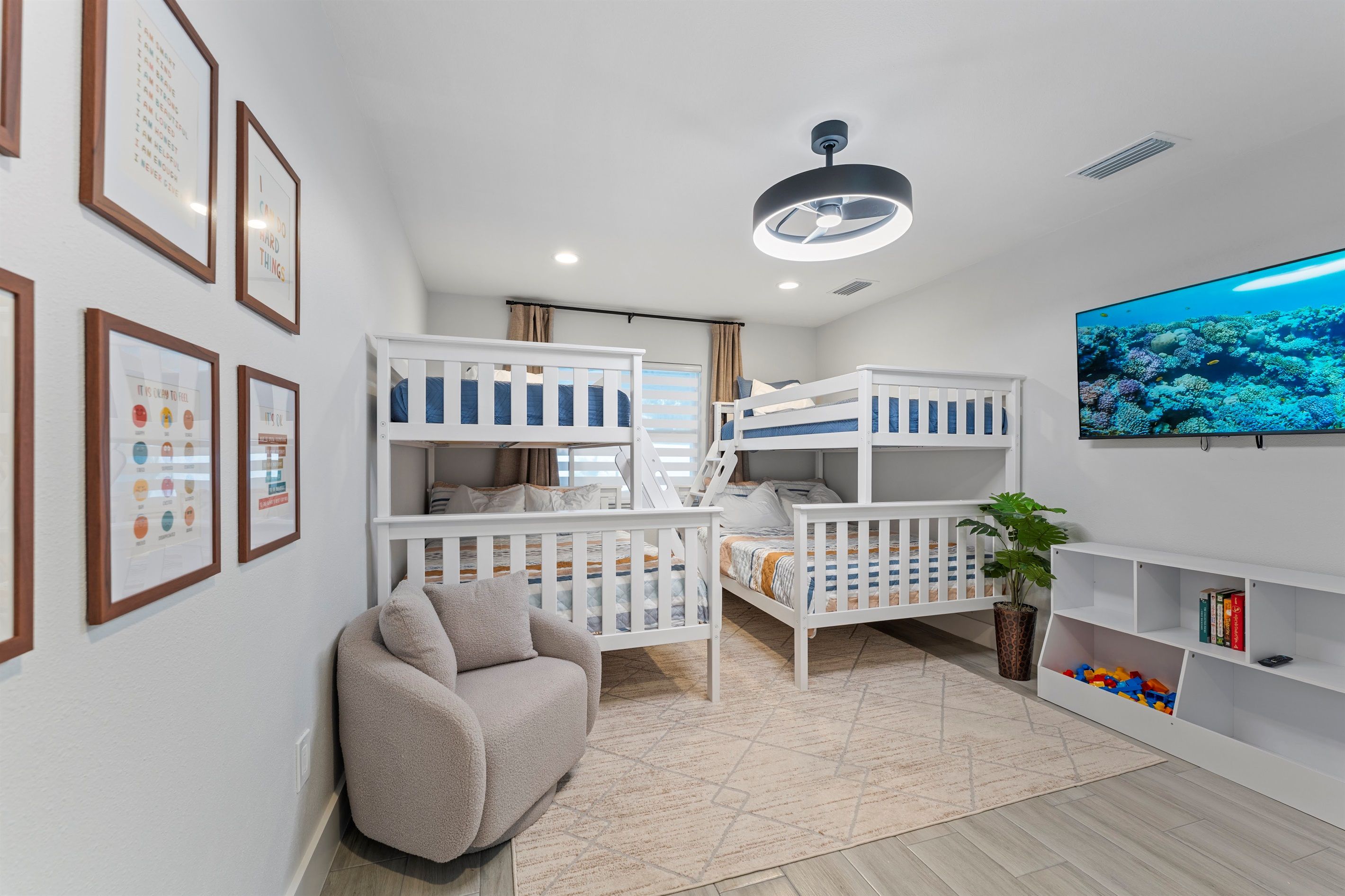 A child-friendly room with bunk beds, a sofa, a TV, and framed pictures on the wall.