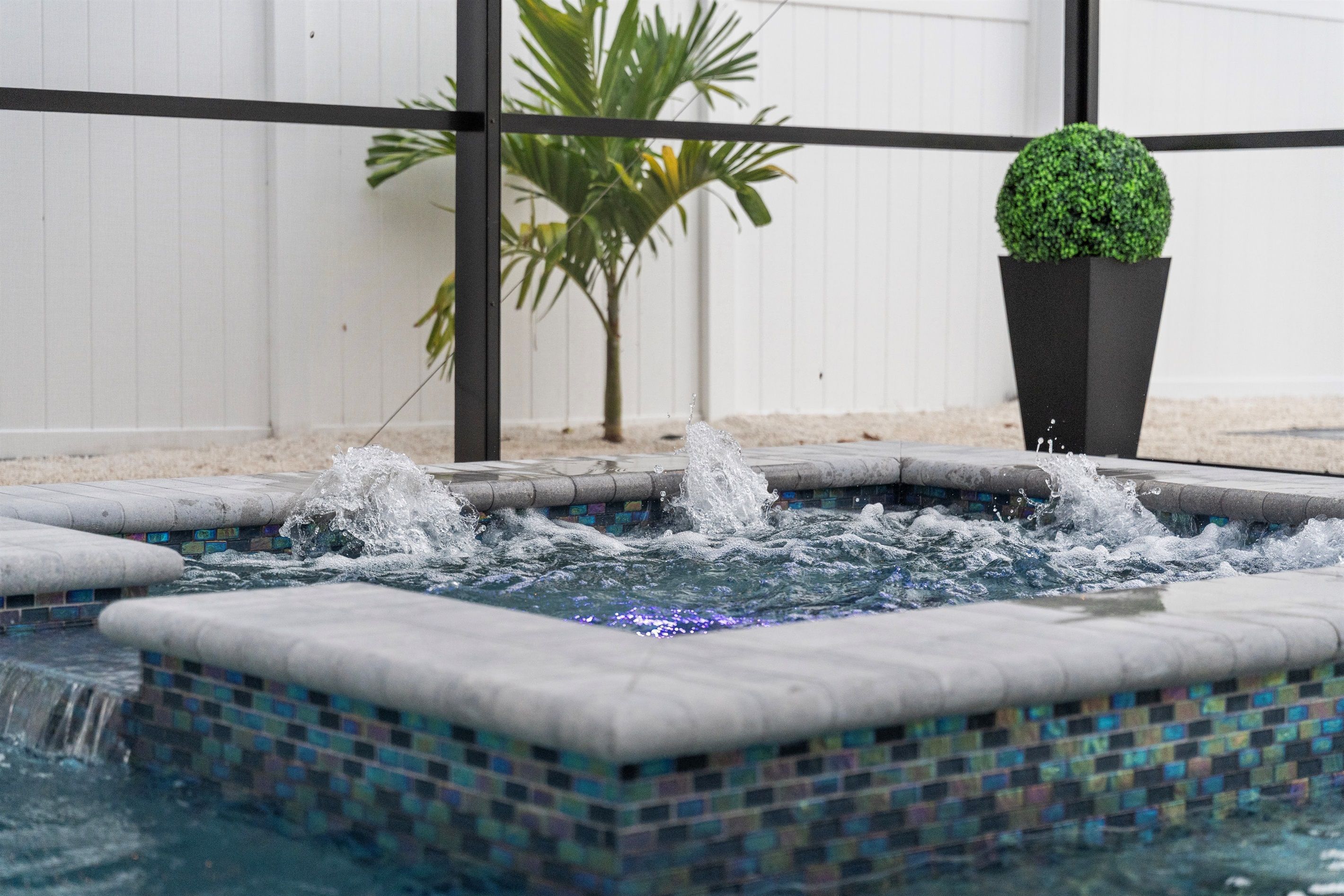 Un petit bain à remous carrelé, doté de jets d’eau, entouré d’une clôture blanche et agrémenté d’une plante en pot.