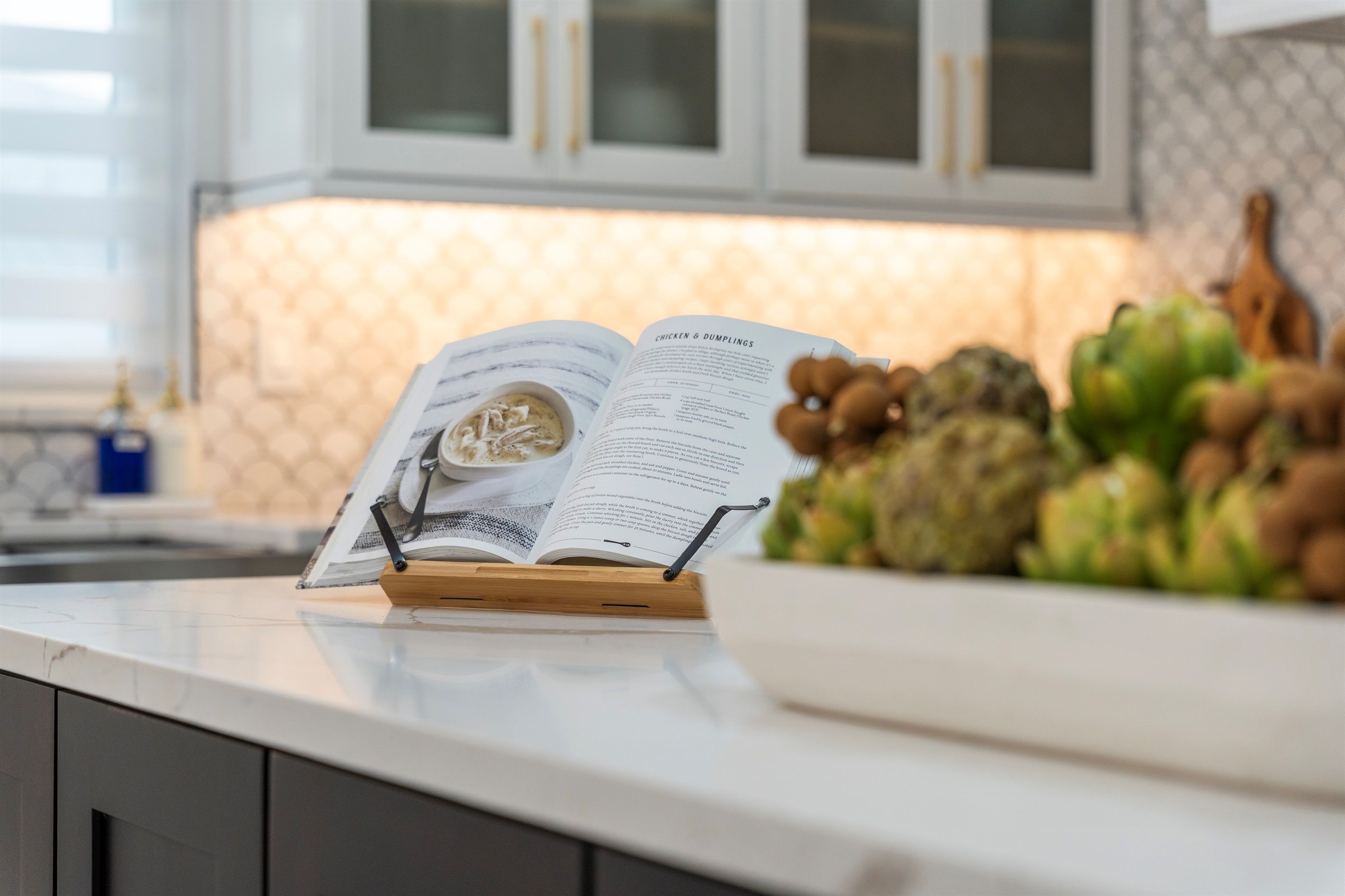 A kitchen counter with an open cookbook titled "Chicken & Dumplings" and a bowl of vegetables.