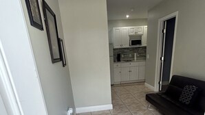 Um corredor com um tapete de entrada preto, uma porta branca e um sofá preto em uma sala de estar.