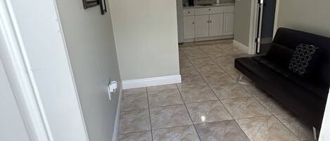 A hallway leading to a kitchen with white cabinets, a black sofa, and a welcome mat.