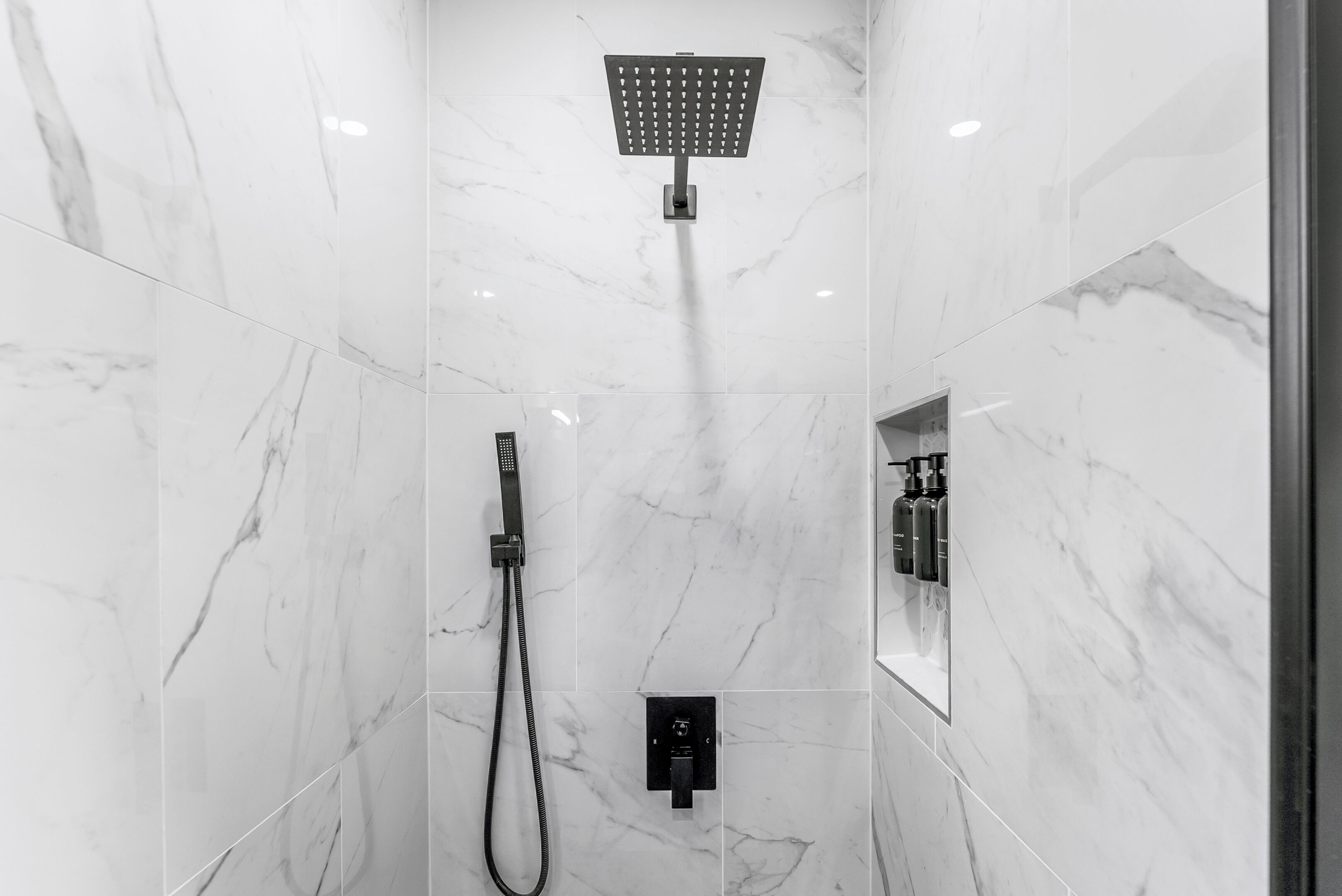 A modern bathroom with a shower, a handheld showerhead, and a control panel.