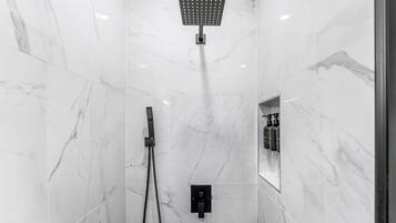 A modern bathroom with a shower, a handheld showerhead, and a control panel.