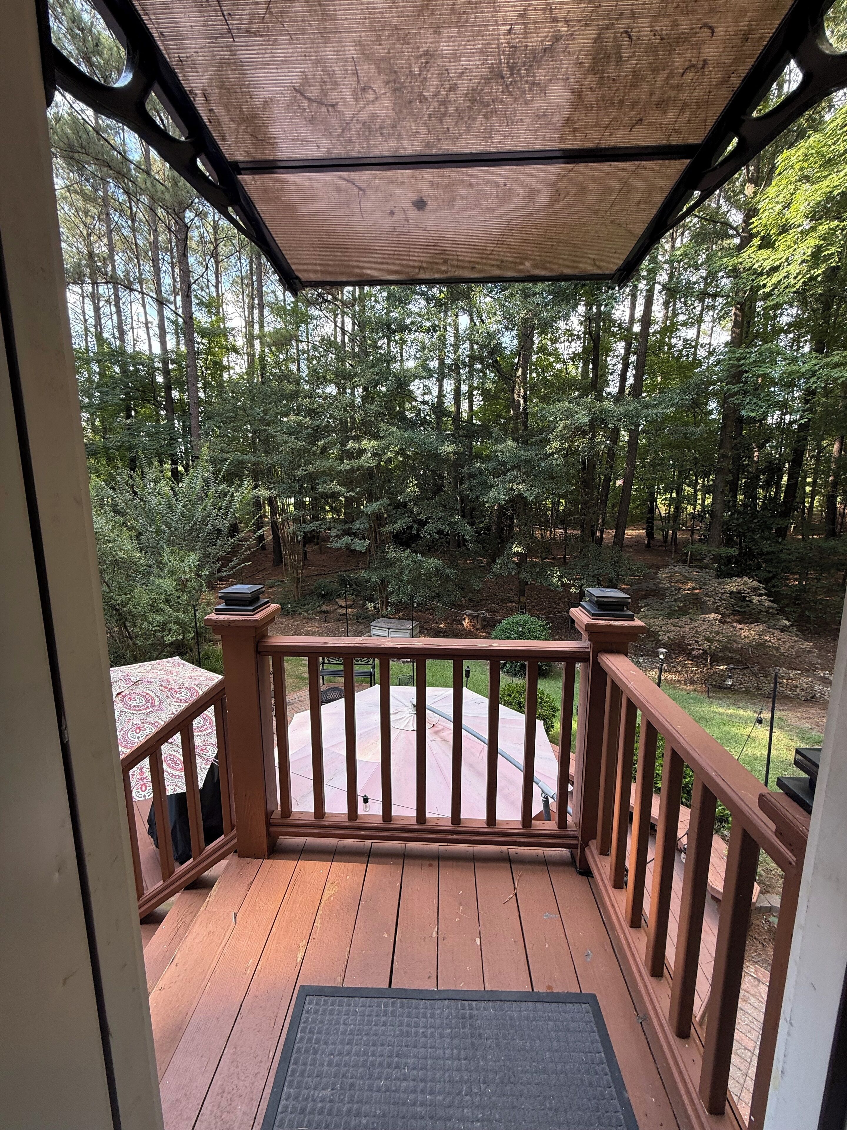 A wooden deck with a pergola overhead, surrounded by a forested area.