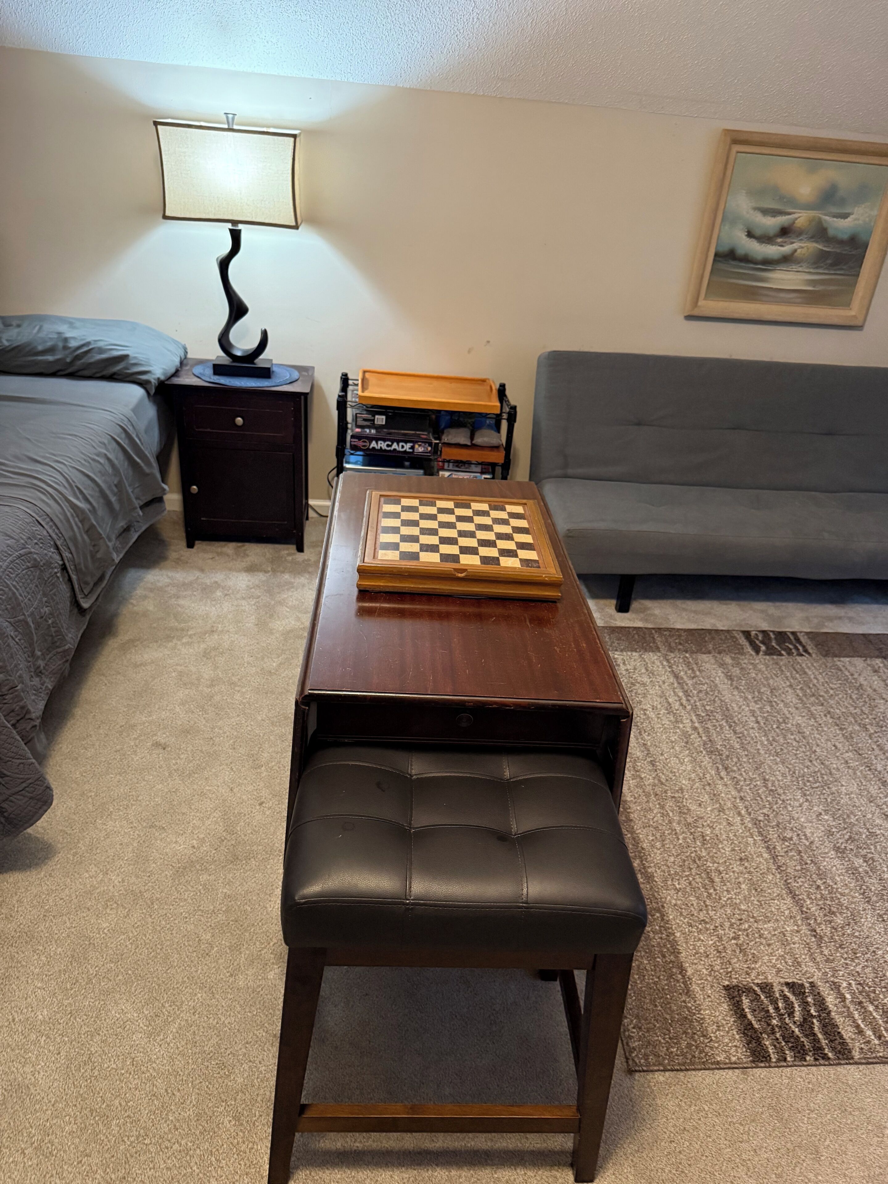 A room with a bed, a small table with a chessboard, a bench, a lamp, and a couch.